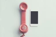 Comparison of a vintage pink telephone receiver and a modern smartphone on a simple backdrop.